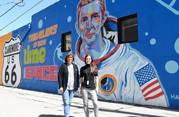 Tanya Andrews, Director of Visit Claremore, and Kelsey Hildebrand, Director of Education and Outreach, standing in front of the mural of Stewart Roosa, Claremore’s own astronaut, who piloted the Apollo 14 mission in 1971.