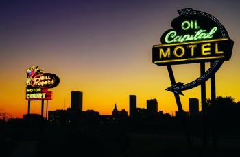 Capital Motel and Will Rogers Motor Court Signs. Historic neon signs illuminate the Tulsa skyline at sunset. This photograph was selected as part of the USPS Route 66 Centennial stamp pane, helping bring the spirit of Route 66 to millions of Americans. © David J. Schwartz / Pics on Route 66.