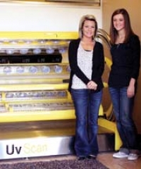 Tanning salon manager Megan Shelton, left, and Morgan Roberts, store employee, stand beside one of the high-pressure tanning beds available at Owasso’s Touch of Sun.