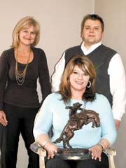 Jenks Chamber of Commerce staff Annette Bowles, president, Josh Driskell, director of communications and public affairs, and Tracie O’Banion (seated), ­director of member services, show a Remington bronze statue that will be included in their first-ever live auction at Buckskin, Boots &amp; BBQ.