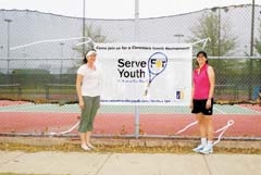 Mendy Stone (left) and Liz Cary hang the Serve for Youth banner at Claremore’s high school tennis courts.