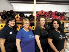 Devon Chezem, Lucy Duwel, Rhonda Hinton, and Tina Hastings stand in front of the large variety of nylon colors available at WaveOn Flags &amp; Banners.