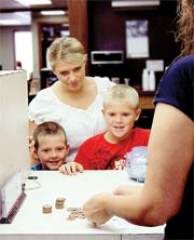 Through RCB Bank Kids Club, Mom Amber Holloway teaches her sons Kohl (right) and Dakota about saving money.