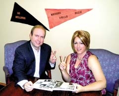 Classmates Jake (actor David Barron) and Elizabeth (actress Celina Davis) each flash peace signs while reminiscing over their 1960 yearbook from Neosho Falls High School. They are two of the seven class members known as \"The Lucky Seven.\"