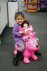 Sitting on a pink Wahoo dog, three-year-old Tayla Vance hugs a Madame Alexander Playful Petals doll.